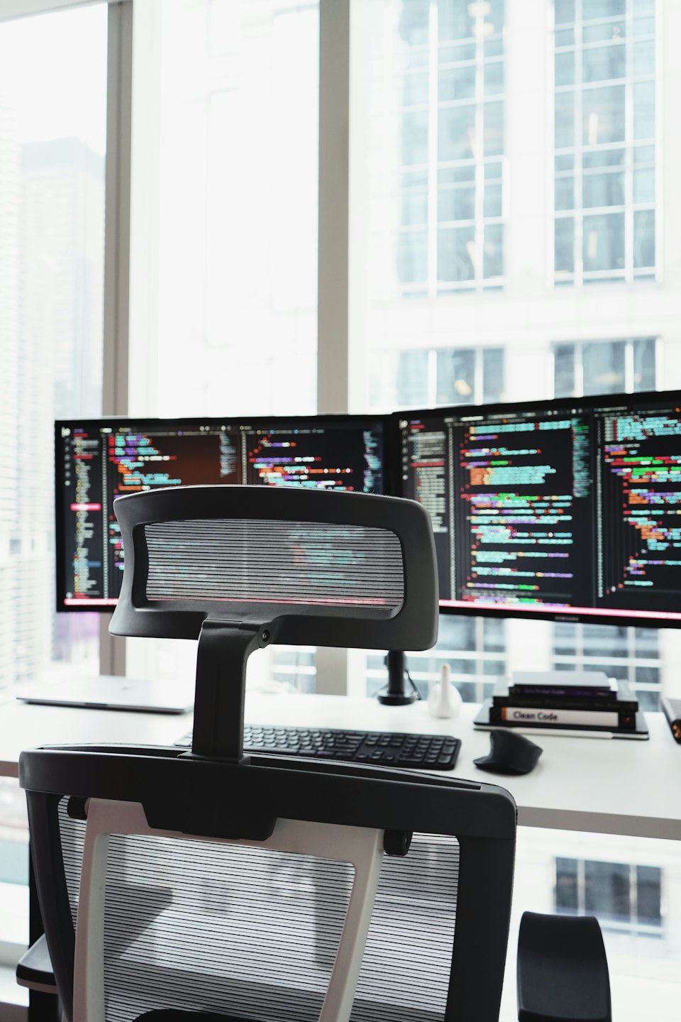 Two computer monitors showing code on a white desk.